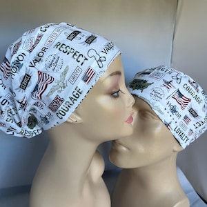 May include: Two white scrub hats with a patriotic theme. The hats feature red, white, and blue American flags, stars, and words like "honor", "courage", "respect", and "loyalty".