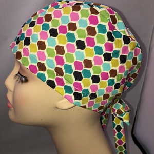 May include: A colorful patterned surgical scrub hat with a long tie. The pattern features a repeating geometric design in shades of brown, green, pink, blue, and white.