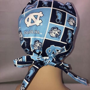 Pu&ograve; includere: Cappello chirurgico blu e bianco con motivo a Carolina Tar Heels e il testo "Carolina TM".