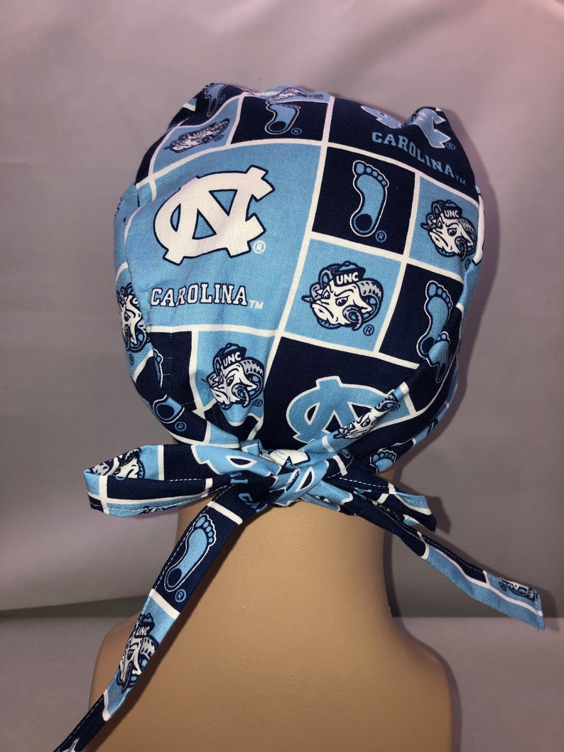 Pu&ograve; includere: Cappello chirurgico blu e bianco con motivo a Carolina Tar Heels e il testo "Carolina TM".