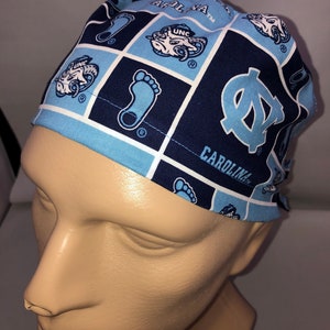 Pu&ograve; includere: Un berretto chirurgico blu e bianco con motivo a fantasia con il testo "Carolina" e "UNC" su di esso.