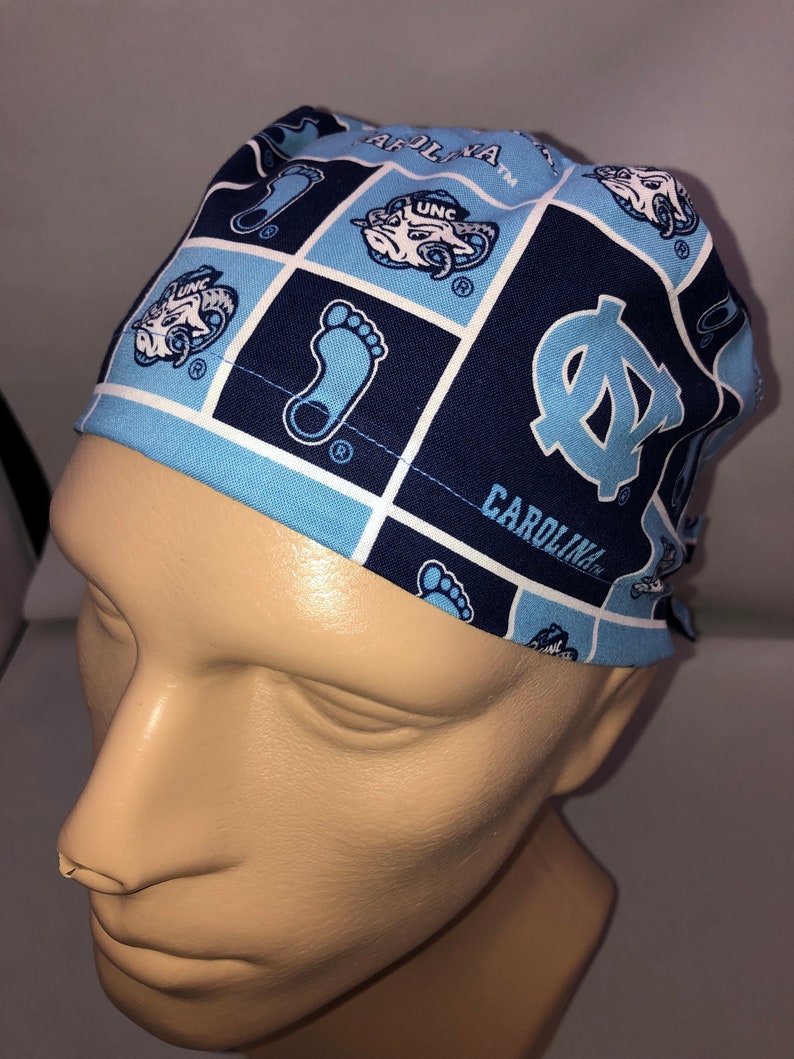 Pu&ograve; includere: Un berretto chirurgico blu e bianco con motivo a fantasia con il testo "Carolina" e "UNC" su di esso.