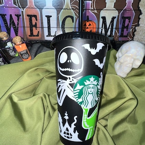 Puede incluir: Taza reutilizable negra con un dise&ntilde;o blanco que presenta al personaje Jack Skellington de la pel&iacute;cula Pesadilla antes de Navidad, un logotipo de Starbucks y murci&eacute;lagos. La taza tiene una tapa verde y una pajita.