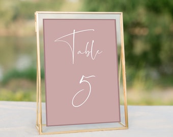 May include: A gold-framed table number sign with a dusty rose background and white calligraphy that reads "Table 5".