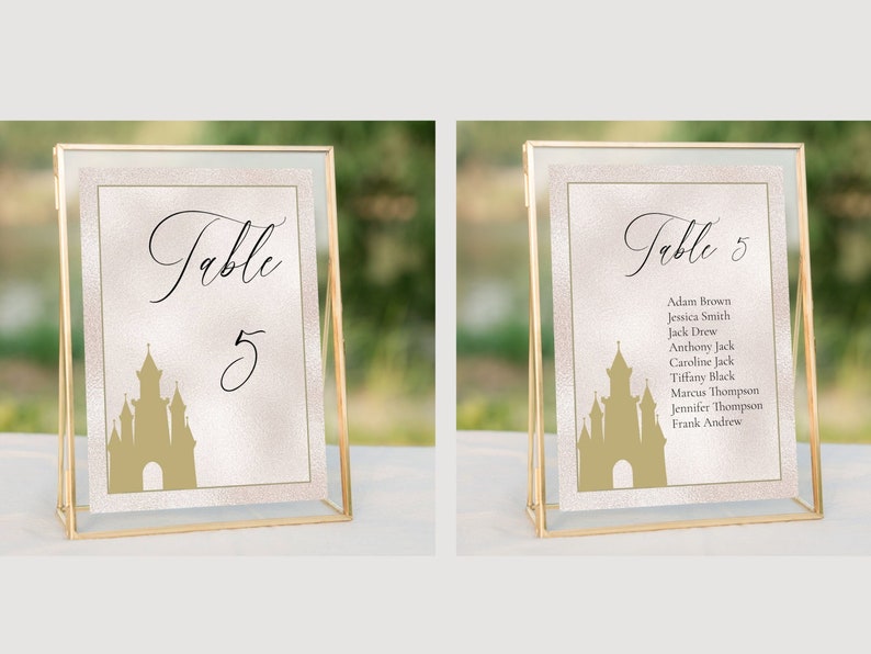 K&ouml;nnte beinhalten: Zwei goldgerahmte Tischnummernschilder mit einer Schlosssilhouette und dem Text "Tisch 5". Das Schild rechts listet auch die Namen der G&auml;ste auf, die dem Tisch zugewiesen sind.