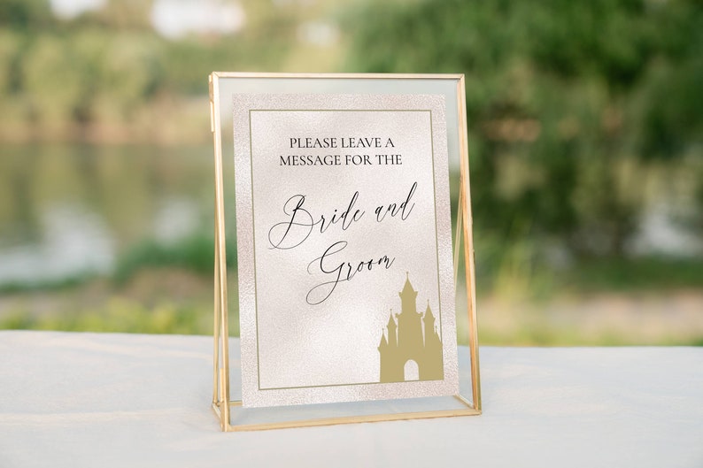 K&ouml;nnte beinhalten: Ein goldfarbener Rahmen mit einem wei&szlig;en Hintergrund und goldenem Glitzer. Das Schild sagt "Bitte hinterlassen Sie eine Nachricht f&uuml;r das Brautpaar" mit einer goldenen Silhouette eines Schlosses.