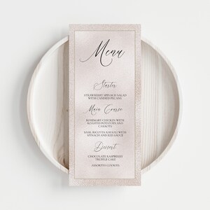 K&ouml;nnte beinhalten: Eine rosa und goldene Speisekarte mit dem Wort "Menu" in Kursivschrift. Die Speisekarte listet einen Vorspeise, ein Hauptgericht und ein Dessert auf. Die Vorspeise ist ein Erdbeer-Spinat-Salat mit kandierten Pekann&uuml;ssen. Das Hauptgericht ist Rosmarin-H&uuml;hnchen mit Bratkartoffeln und Karotten, Basilikum-Ricotta-Ravioli mit Spinat und roter Sauce. Das Dessert ist Schokoladen-Himbeer-Tr&uuml;ffelkuchen und verschiedene Kekse.