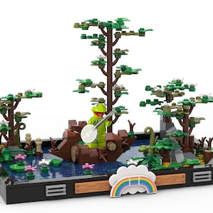 Könnte beinhalten: Eine grüne Froschpuppe spielt Banjo in einem Holzboot auf einem blauen See mit grünen Bäumen und einem Regenbogen. Die Szene ist mit Lego-Steinen gebaut.