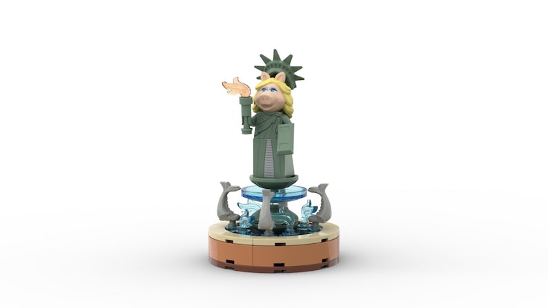 Puede incluir: Una figura de Lego verde y marr&oacute;n de Miss Piggy vestida como la Estatua de la Libertad, de pie sobre una base de fuente con agua azul y figuras de delfines grises.