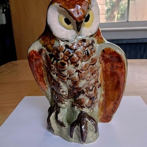 May include: A ceramic owl figurine with brown, green, and white glaze. The owl has a detailed face with yellow eyes and a textured body.