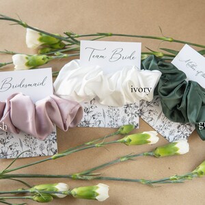 May include: Three satin scrunchies in blush, ivory, and green colors, with corresponding cards that read "bridesmaid", "Team Bride", and "Mother of the Bride".