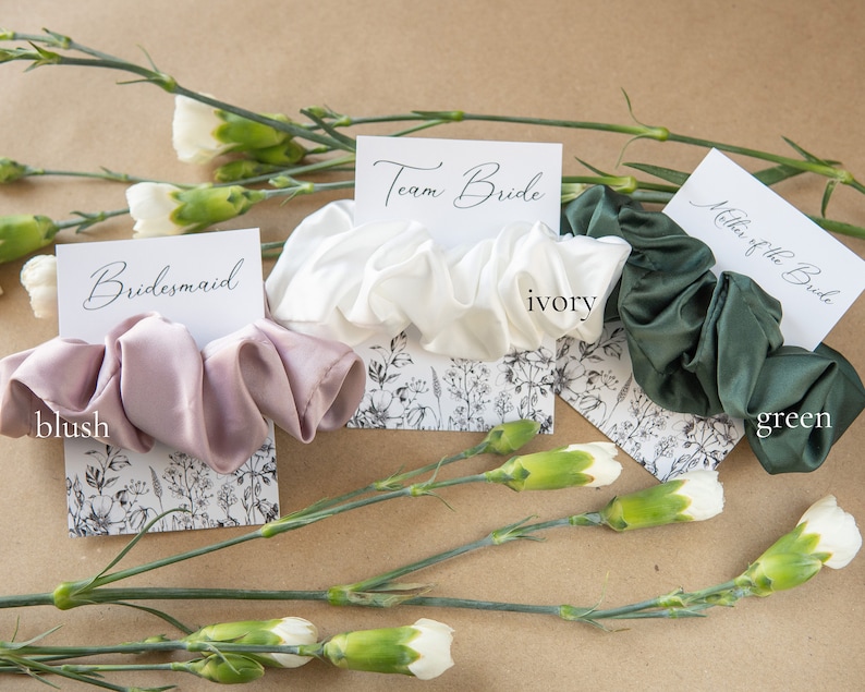 May include: Three satin scrunchies in blush, ivory, and green colors, with corresponding cards that read "bridesmaid", "Team Bride", and "Mother of the Bride".