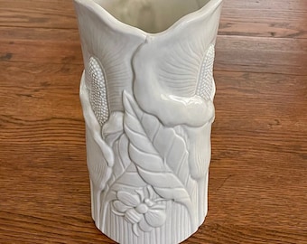 May include: White ceramic vase with an embossed floral design. The vase has a wide mouth and a rounded bottom.