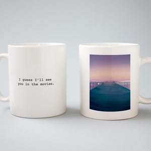 May include: Two white ceramic mugs with a quote on one and a photo of a pier on the other. The quote reads "I guess I'll see you in the movies."