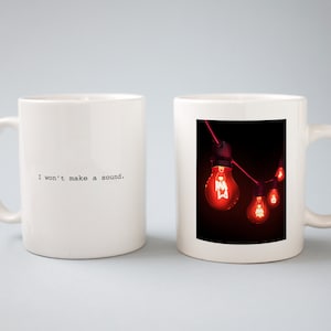 May include: Two white ceramic mugs. One mug has the text "I won't make a sound." printed on it. The other mug has a photo of a string of red light bulbs.