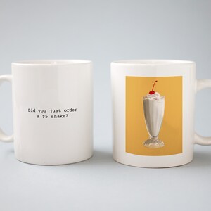 May include: Two white ceramic mugs with black text. One mug says "Did you just order a $5 shake?" The other mug has a picture of a milkshake with whipped cream and a cherry on top.