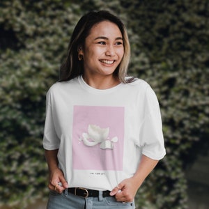 Pode incluir: Camiseta branca com um gráfico quadrado rosa que apresenta uma casca de ovo quebrada em um fundo rosa. O texto "like a good girl." é impresso abaixo do gráfico.