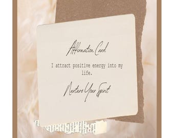 May include: A white card with brown edges and the text "Affirmation Card" at the top. The text "I attract positive energy into my life." is in the middle of the card. The text "Nurture Your Spirit" is at the bottom of the card. The card is on a background of white feathers.