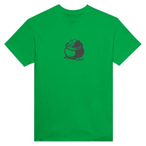 Puede incluir: Una camiseta verde brillante con un gráfico de una olla de oro. La olla es de color gris oscuro y está llena de monedas de oro. La camiseta está hecha de un material suave y tiene mangas cortas.