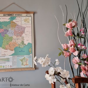 Może przedstawiać: Wizerunek vintage'owej mapy Francji zatytułowanej "La France Metropolitaine" wiszącej na ścianie. Mapa jest wydrukowana na jasnoniebieskim tle z kolorowymi granicami dla każdego regionu. Mapa jest oprawiona w drewniany listek i ma małą etykietę w prawym g&oacute;rnym rogu z napisem "Collection Viacarto".
