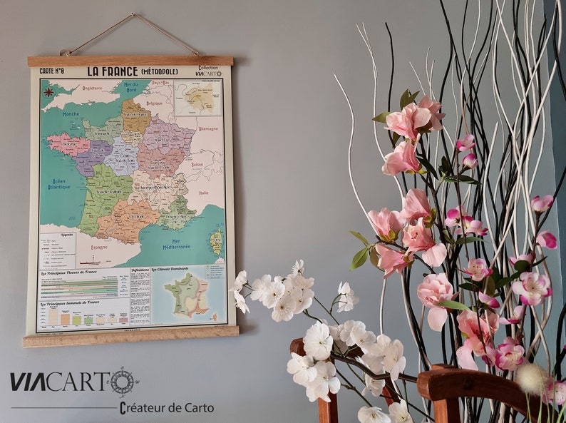 Może przedstawiać: Wizerunek vintage'owej mapy Francji zatytułowanej "La France Metropolitaine" wiszącej na ścianie. Mapa jest wydrukowana na jasnoniebieskim tle z kolorowymi granicami dla każdego regionu. Mapa jest oprawiona w drewniany listek i ma małą etykietę w prawym g&oacute;rnym rogu z napisem "Collection Viacarto".