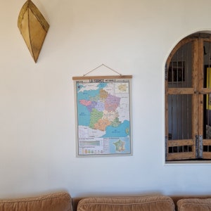 Może przedstawiać: Antyczna mapa Francji zatytułowana "La France (1900-1913)" wisi na białej ścianie. Mapa jest podzielona na regiony i wydrukowana w r&oacute;żnych kolorach. Mapa jest oprawiona w drewnianą ramę i wisi na sznurku.