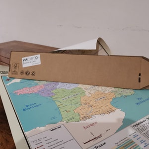 Może przedstawiać: Brązowy kartonowy tubus z nadrukowanym tekstem "VIA CARTO" i logo. Tubus leży na mapie Francji z widocznym tekstem "Ocean Atlantique" i "Espagne".