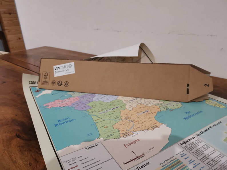 Może przedstawiać: Brązowy kartonowy tubus z nadrukowanym tekstem "VIA CARTO" i logo. Tubus leży na mapie Francji z widocznym tekstem "Ocean Atlantique" i "Espagne".
