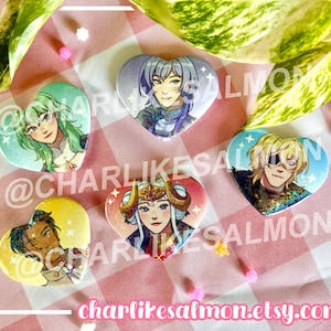 May include: Five heart-shaped pinback buttons featuring colourful anime-style character illustrations. The designs include figures with green, blue, blonde, dark, and white hair, each accented with small white sparkles against vibrant backgrounds.