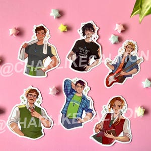 May include: A collection of six stickers featuring stylized illustrations of male characters. The characters are depicted in various outfits and poses, with some holding objects like a guitar or a coffee cup. The stickers are arranged on a pink surface with origami stars.