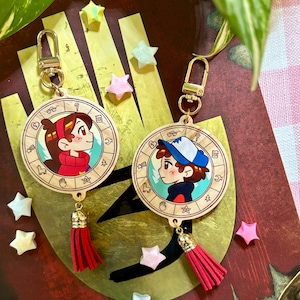 May include: Two wooden keychains featuring cartoon characters, each with a red tassel and gold-colored hardware. One keychain depicts a girl in a red sweater, and the other shows a boy in a blue hat. The keychains are surrounded by star-shaped decorations.