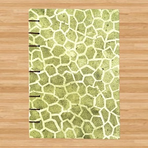May include: A green and white patterned notebook with a stitched binding. The notebook has a textured, almost animal print-like pattern.