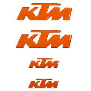 Puede incluir: Cuatro calcomanías con el logotipo KTM naranja de diferentes tamaños están dispuestas verticalmente sobre un fondo blanco. El logotipo KTM presenta letras estilizadas, con la 'K' y la 'M' conectadas por una barra horizontal.