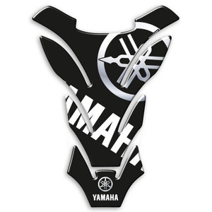 Op de afbeelding: Zwarte en witte Yamaha motorfiets tankbeschermer met het Yamaha logo en tekst. De tankbeschermer is gevormd om op de motorfiets tank te passen en heeft een glanzende afwerking.