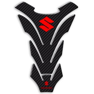 May include: Black carbon fiber motorcycle tank pad with a red Suzuki logo. The pad has a unique design with a pointed bottom and a curved top.