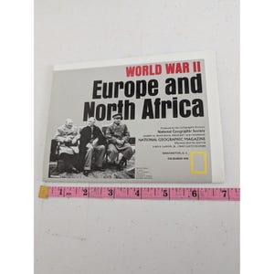 May include: A National Geographic map titled World War II Europe and North Africa, dated December 1991, featuring a black and white photograph of three leaders. A pink measuring tape shows the map width is approximately 7.5 inches wide.