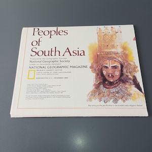 May include: A National Geographic Magazine cover titled "Peoples of South Asia" from December 1984. The cover features an illustration of a person in traditional attire, with text that reads "Boy acting as the god Krishna in the kumbh mela religious festival."