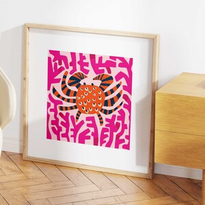 May include: A framed print of a stylized orange crab with black stripes and white eyes on a pink background with pink abstract shapes.