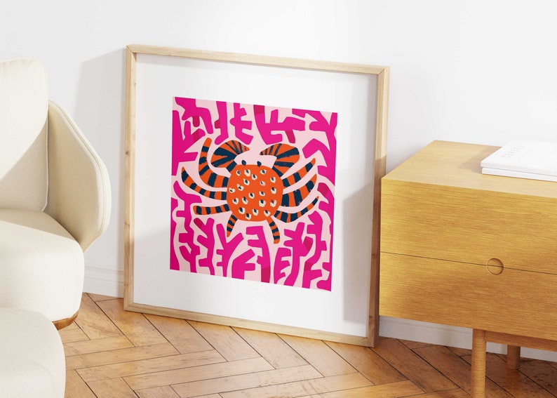 May include: A framed print of a stylized orange crab with black stripes and white eyes on a pink background with pink abstract shapes.