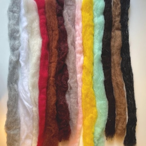 May include: A collection of twelve vertical strips of raw wool roving arranged side by side in a spectrum of colors including gray, white, cream, red, brown, dark maroon, taupe, light pink, bright yellow, mint green, dark brown, and black.