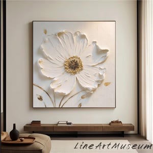 May include: A large, textured white flower art piece with a gold center, set against a white background within a black frame. The artwork features raised petals and delicate gold accents, creating a 3D effect. The artwork is signed "Line Art Museum".