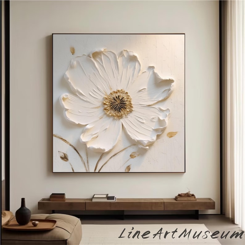 May include: A large, textured white flower art piece with a gold center, set against a white background within a black frame. The artwork features raised petals and delicate gold accents, creating a 3D effect. The artwork is signed "Line Art Museum".