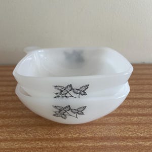 Könnte beinhalten: Zwei weiße, quadratische Schalen, die übereinander gestapelt sind. Jede Schale hat ein schwarzes Blumendesign. Die Schalen bestehen aus glänzendem Material und stehen vor einem neutralen Hintergrund.