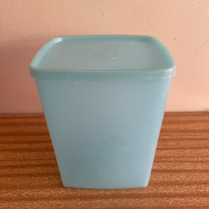 May include: A light blue square plastic container with a lid. The container is empty.