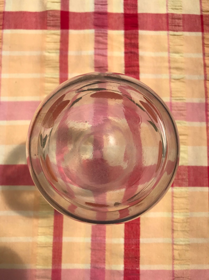 May include: A clear glass object with a rounded bottom and a thick rim. The glass reflects the colors of the plaid fabric beneath it, creating a play of pinks, reds, and yellows. The object appears to be a drinking glass or a similar container.
