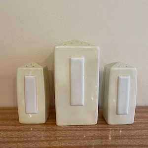 Op de afbeelding: Set van drie witte keramische zout- en peperstrooiers met een rechthoekig ontwerp en een wit rechthoekig label aan de voorkant van elke strooier.