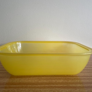 May include: A rectangular yellow glass baking dish with rounded corners and a smooth, translucent finish. The dish features a wide, flat rim extending around the top edge, providing a clear view of the interior basin and the solid yellow base.