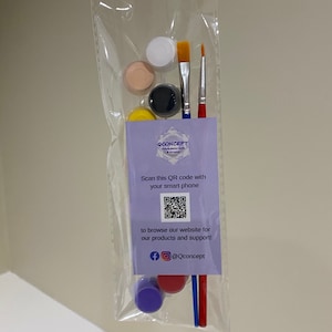 May include: A set of paint pots and brushes in a clear plastic bag. The paint pots are in various colours, including white, beige, black, and yellow. The bag also includes a small card with a QR code and the text "QCONCEPT Unique polymer crafts and art paint".