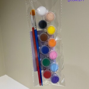 May include: A set of 10 paint pots in a clear plastic bag with two paintbrushes. The paint pots are arranged in a row and contain different colours of paint, including white, black, brown, yellow, orange, pink, green, blue, red, and purple. The paintbrushes are red and blue.
