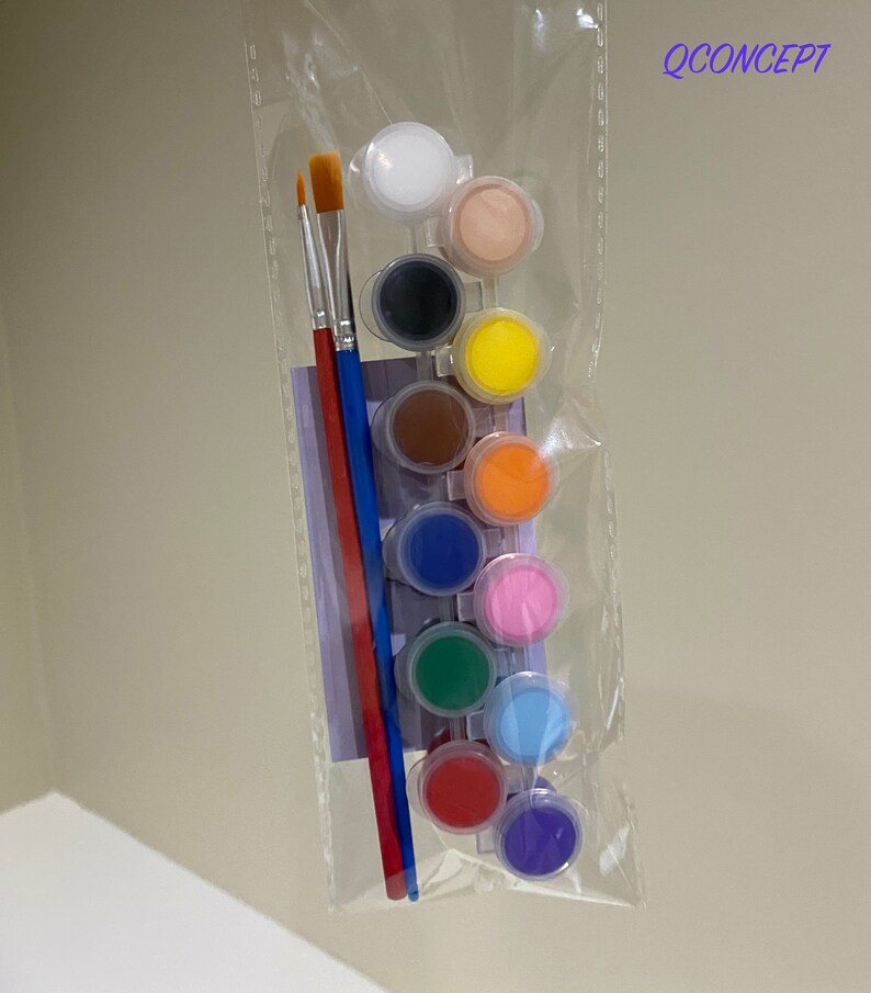 May include: A set of 10 paint pots in a clear plastic bag with two paintbrushes. The paint pots are arranged in a row and contain different colours of paint, including white, black, brown, yellow, orange, pink, green, blue, red, and purple. The paintbrushes are red and blue.